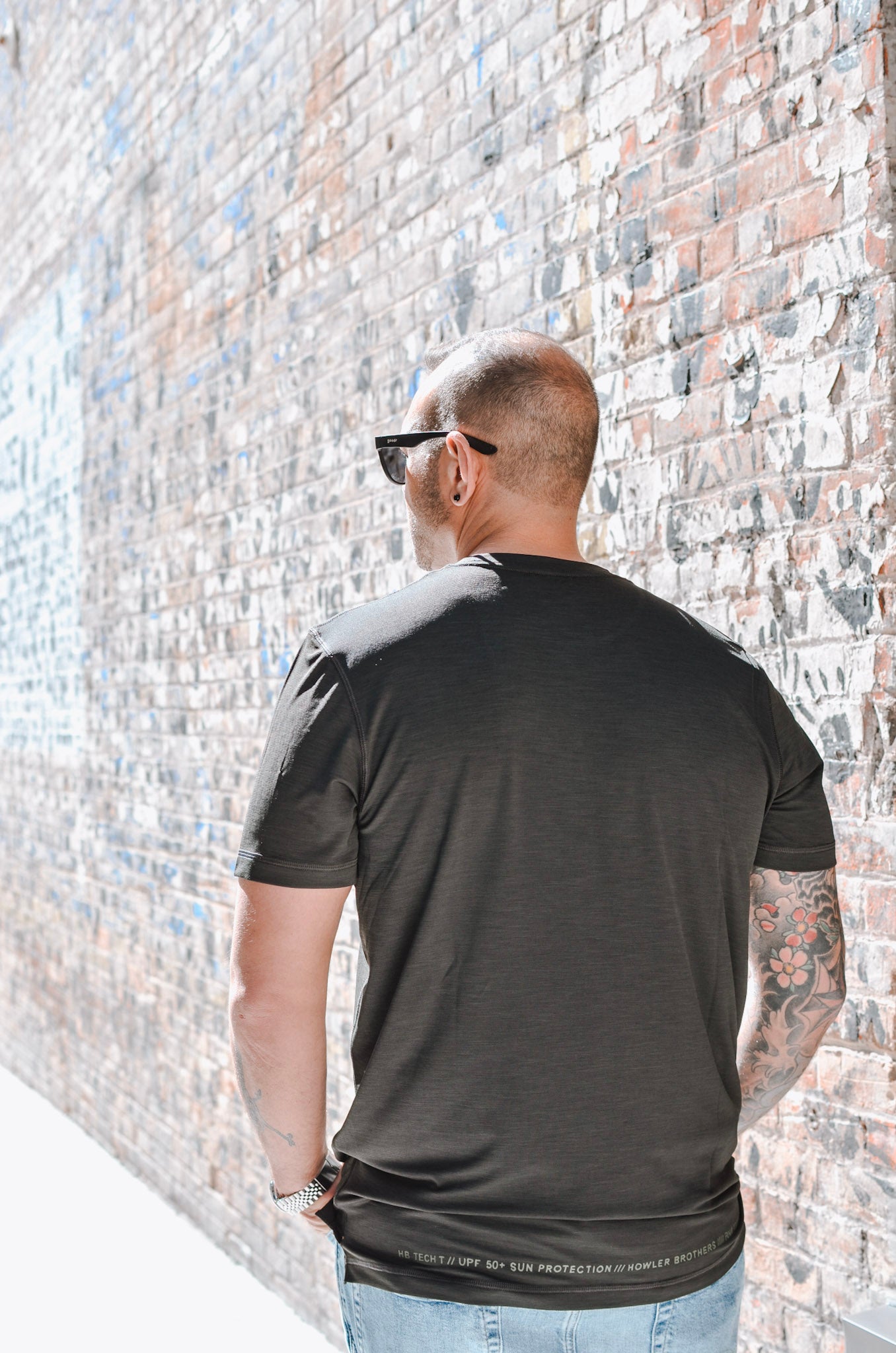 Man wearing a black t-shirt with a white logo against a brick wall.