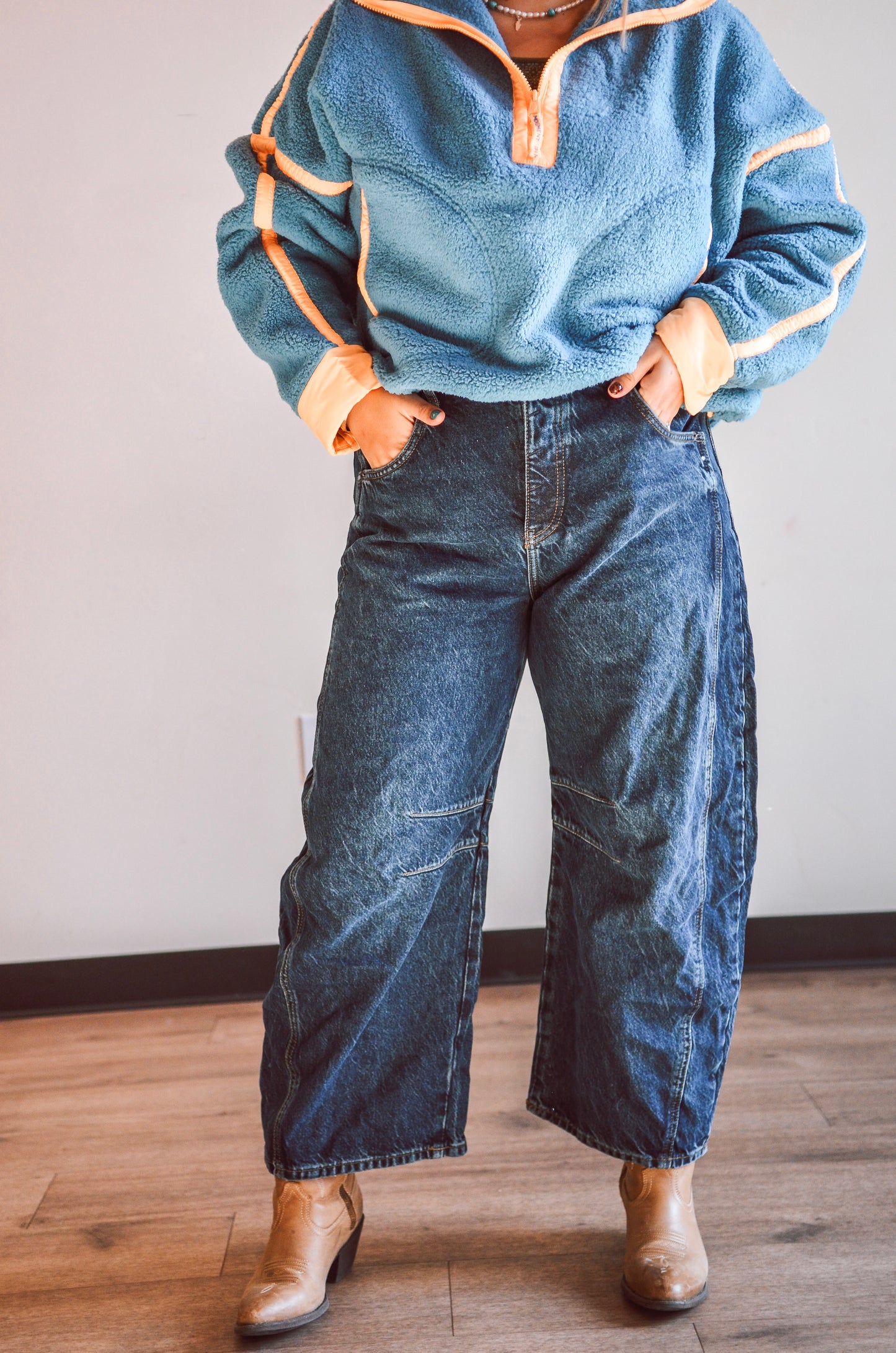 Person wearing a blue fleece pullover with orange trim and blue jeans on a wooden floor.