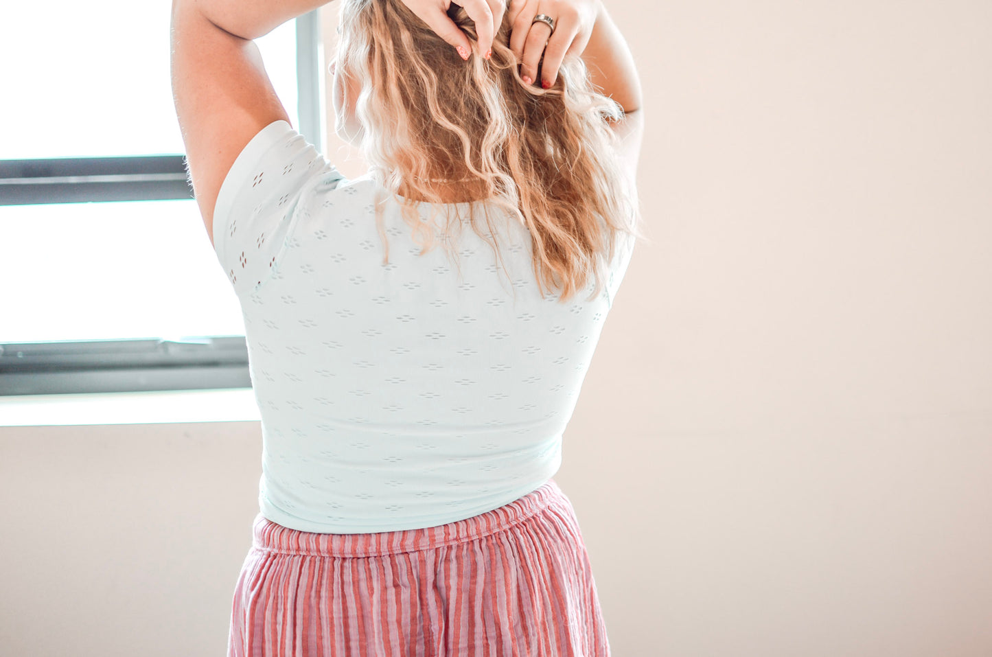 Woman wearing a light blue top and red plaid skirt adjusting her hair indoors.