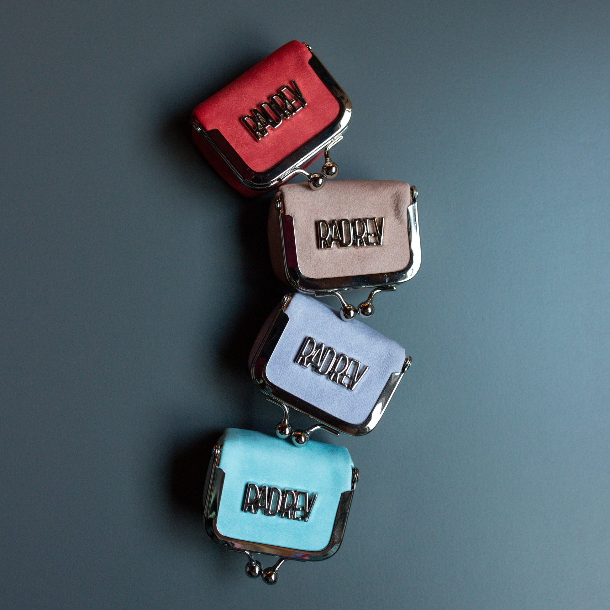 Four small bags in red, beige, blue, and turquoise with 'ADREY' branding on a dark gray background.