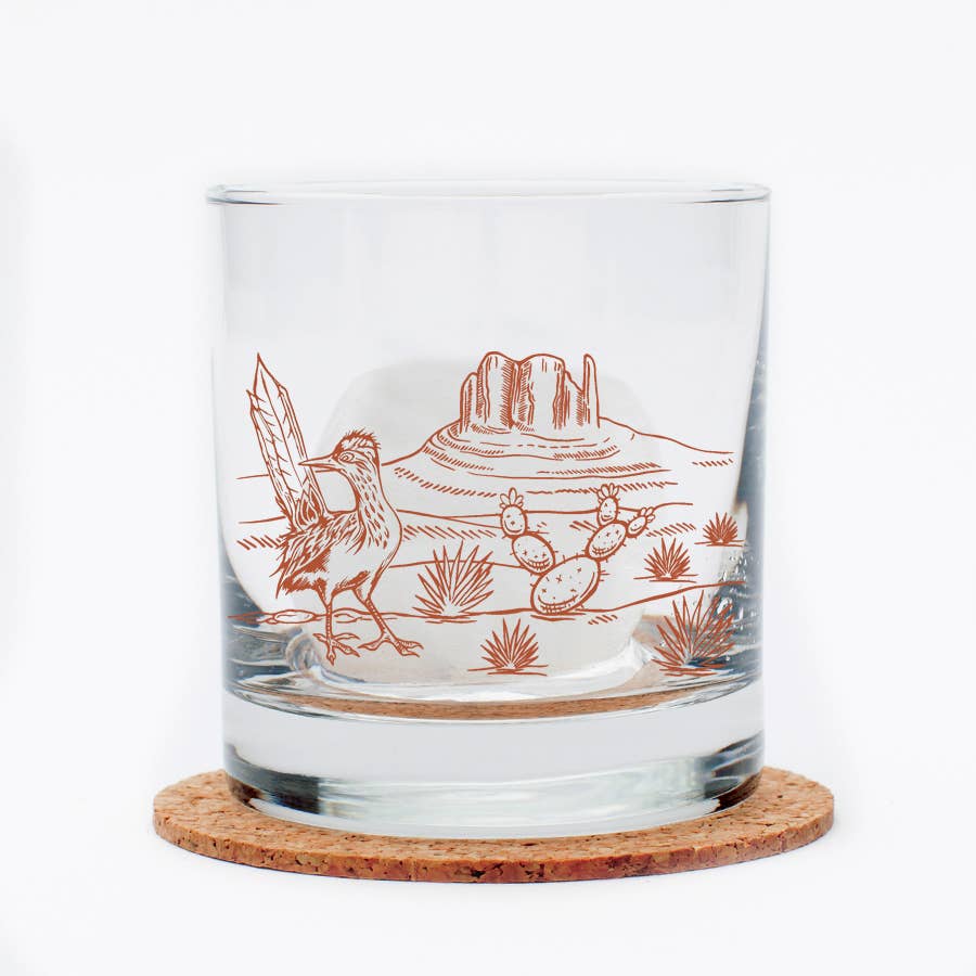 Clear glass tumbler with desert-themed engraving on a cork coaster