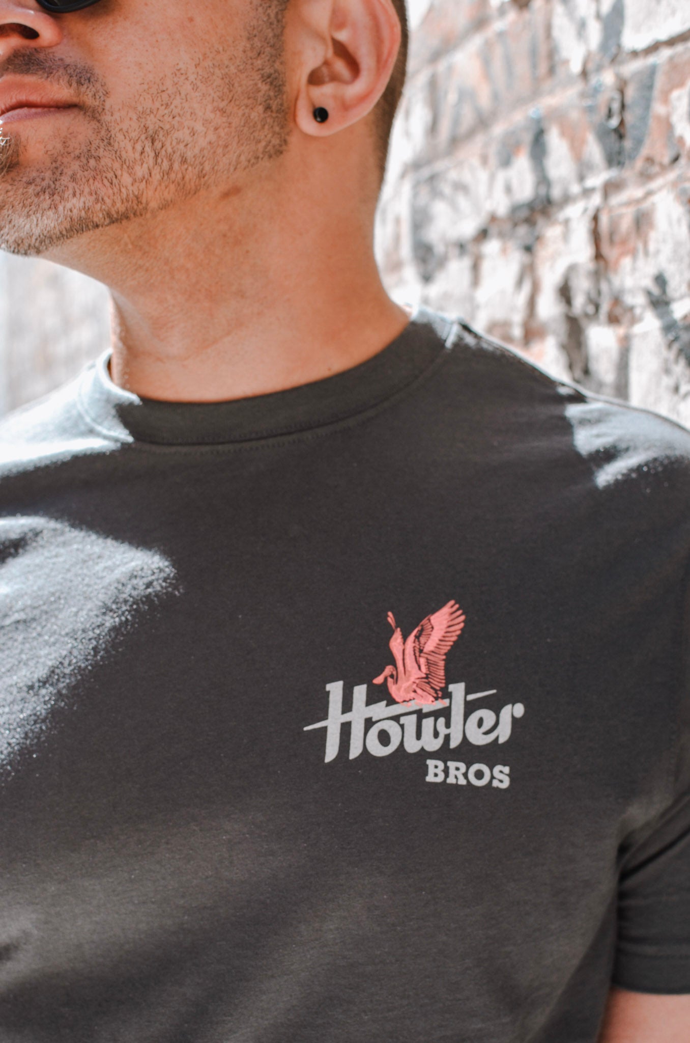 Man wearing a black t-shirt with 'Howler Bros' logo against a brick wall.