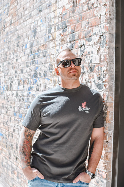 Man wearing a black t-shirt with a logo, standing against a textured brick wall.