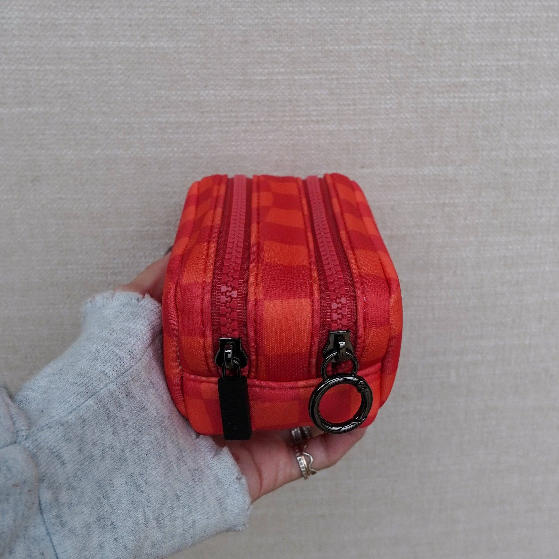 Red checkered pouch with a zipper held by a person against a neutral background