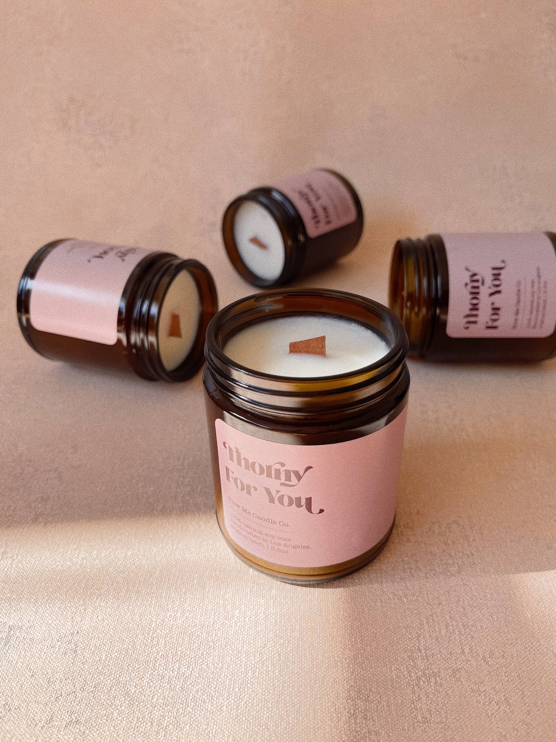 Candle jars with pink labels on a beige surface