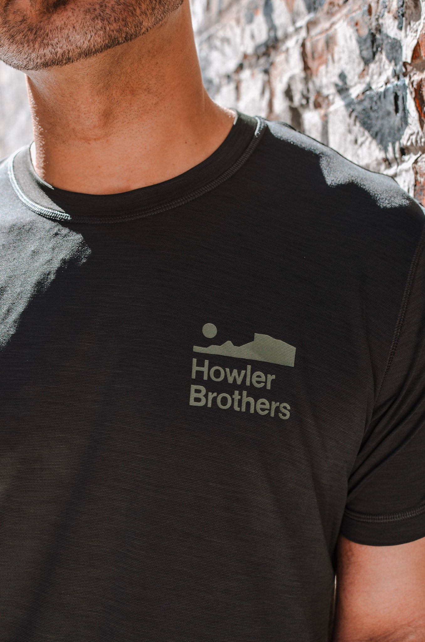 Person wearing a black t-shirt with 'Howler Brothers' logo against a stone wall background
