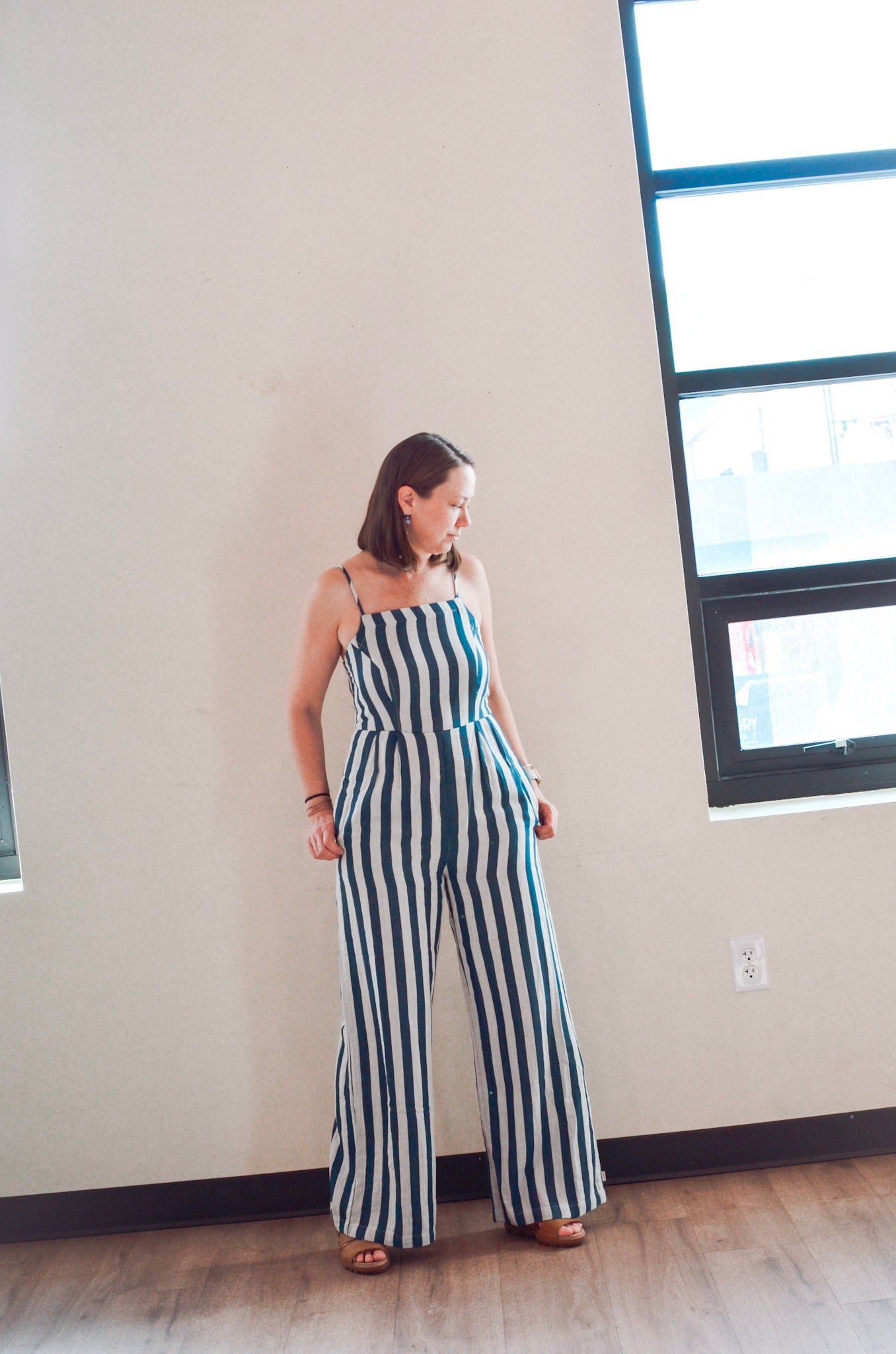 Woman wearing a striped jumpsuit standing in a room with a window.