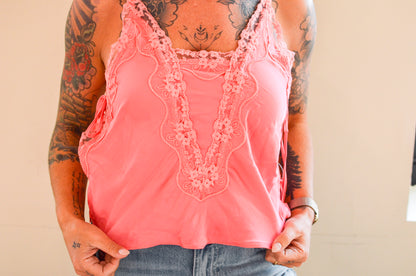 Person wearing a pink lace-trimmed top with tattoos on arms and back.