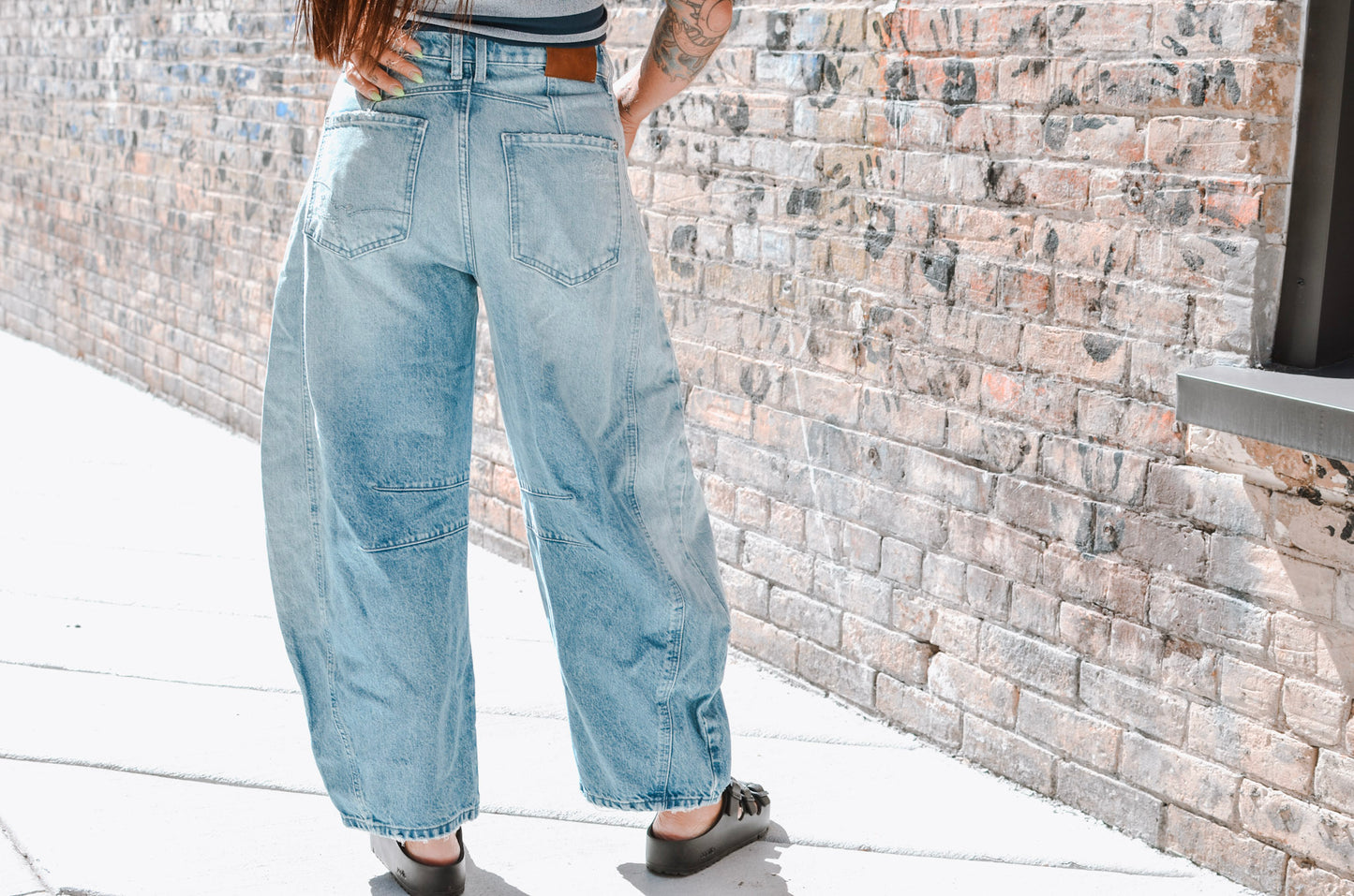 Person wearing light blue jeans standing against a brick wall.