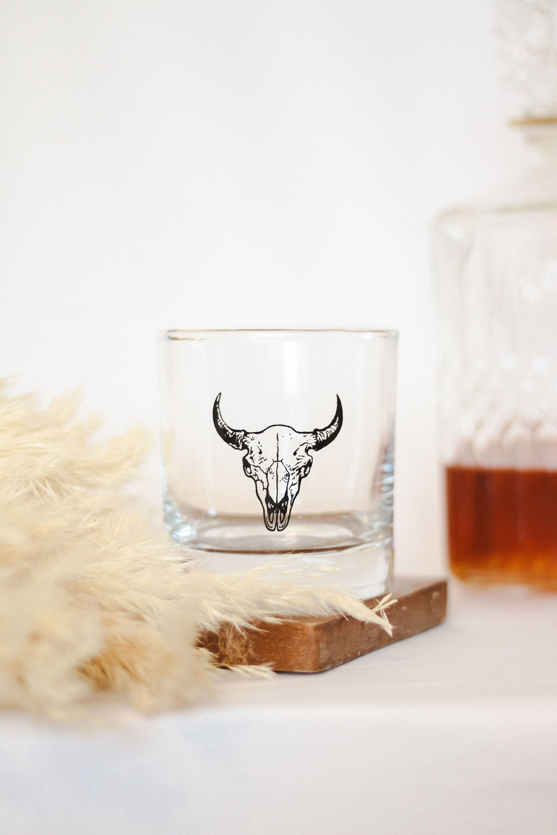 Clear glass with bull skull design on a wooden coaster with a soft white background