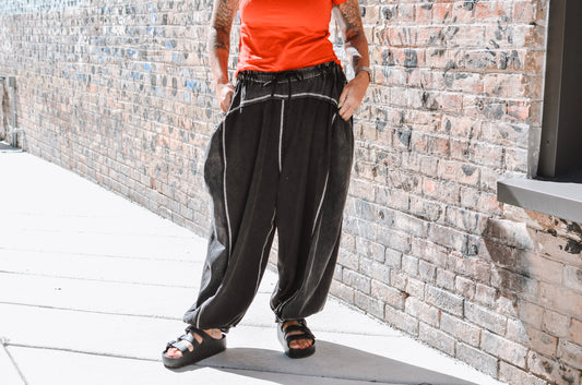 Person wearing black pants with white stripes standing against a stone wall.
