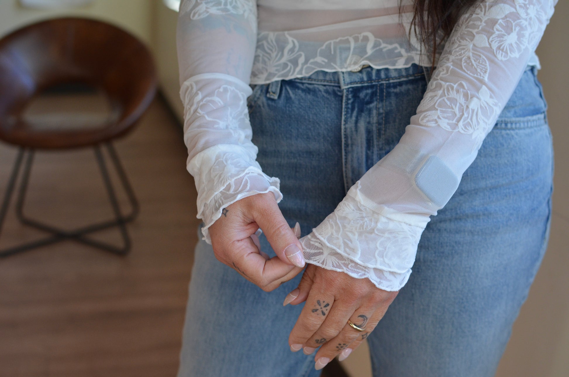 Person wearing a sheer lace long-sleeve top with blue jeans indoors.