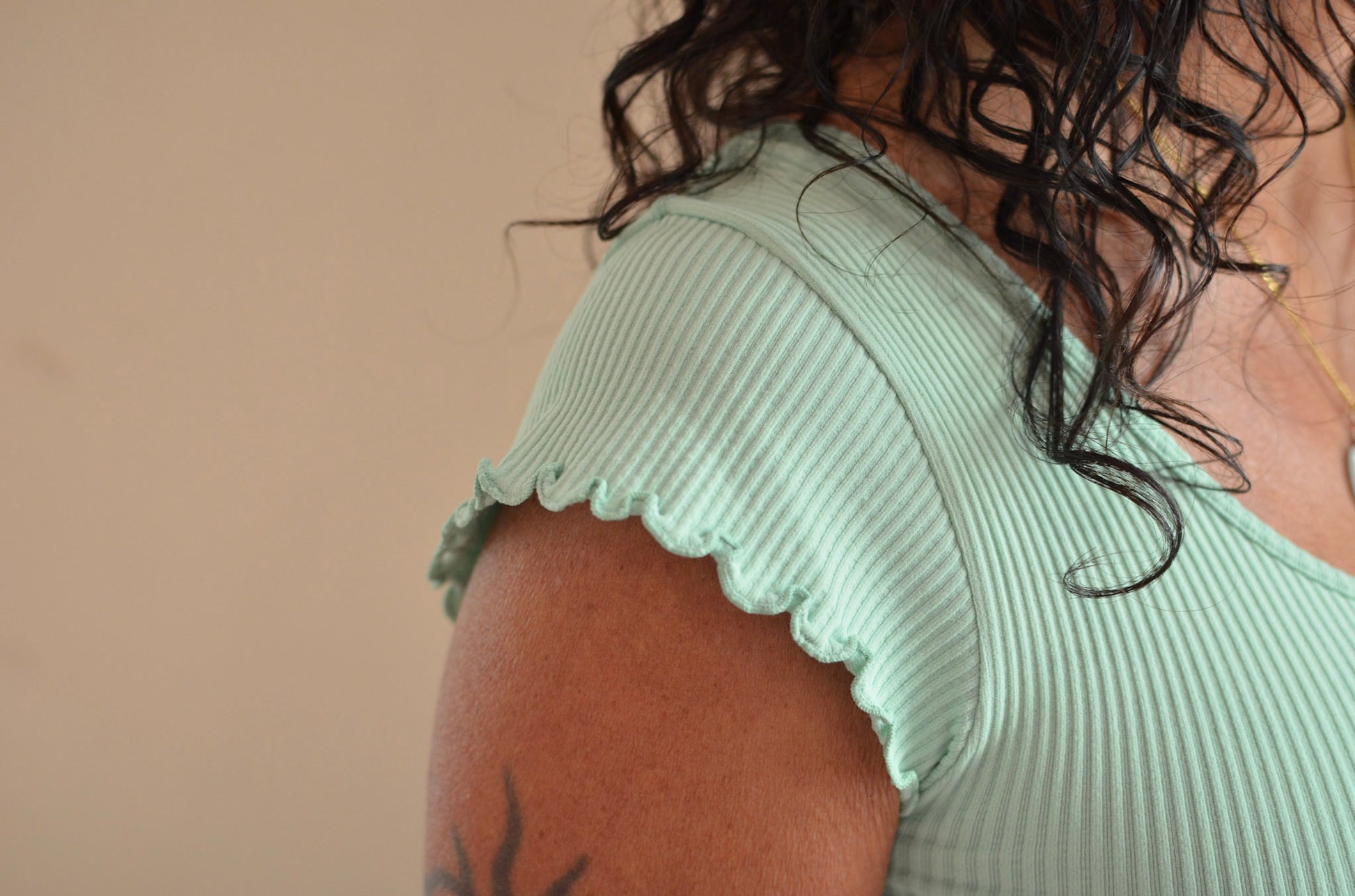 Person wearing a light green ribbed top with ruffled sleeves against a beige background