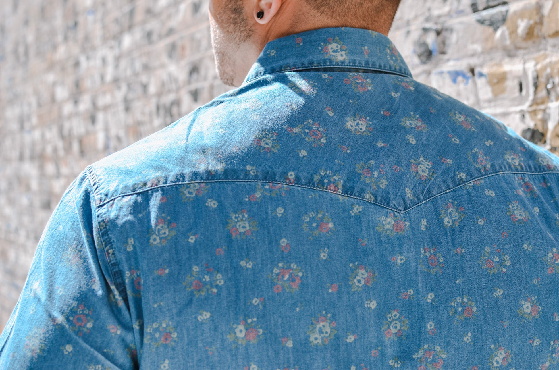 Person wearing a blue floral shirt with a stone wall background