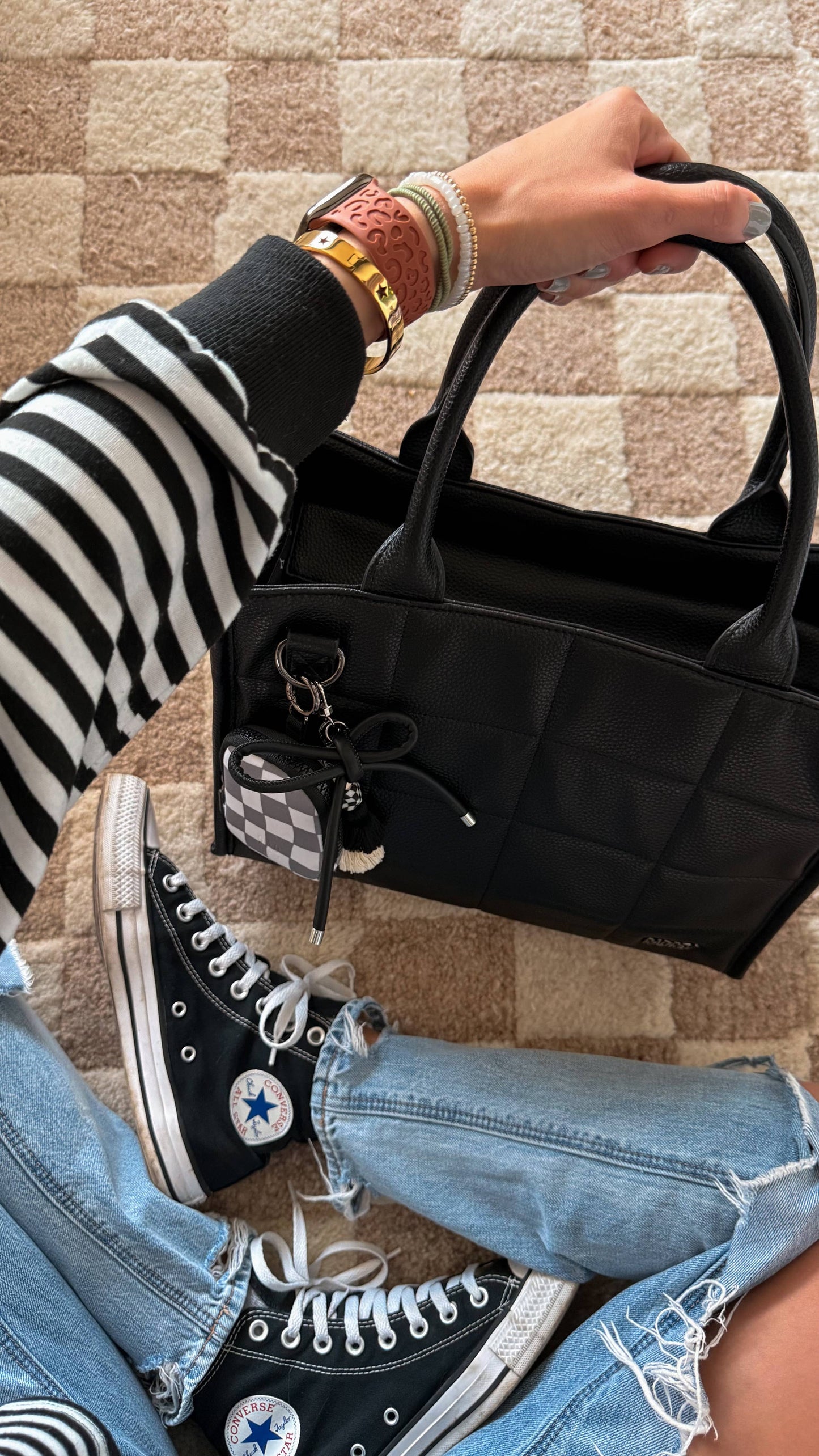 Person holding a black handbag with Converse shoes and striped socks visible.