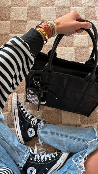 Person holding a black handbag with Converse shoes and striped socks visible.