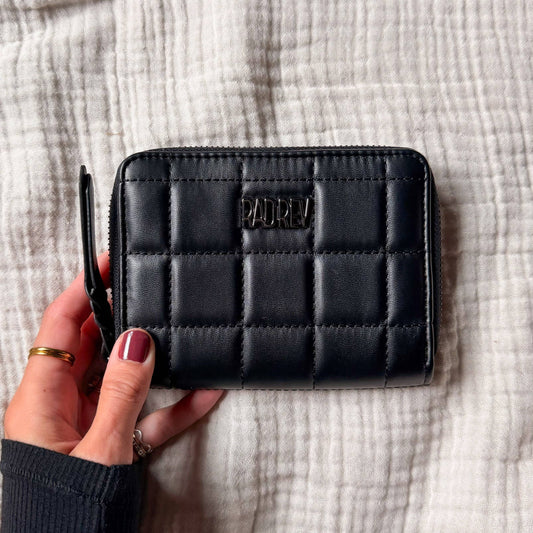 Black quilted wallet held by a hand on a textured fabric background