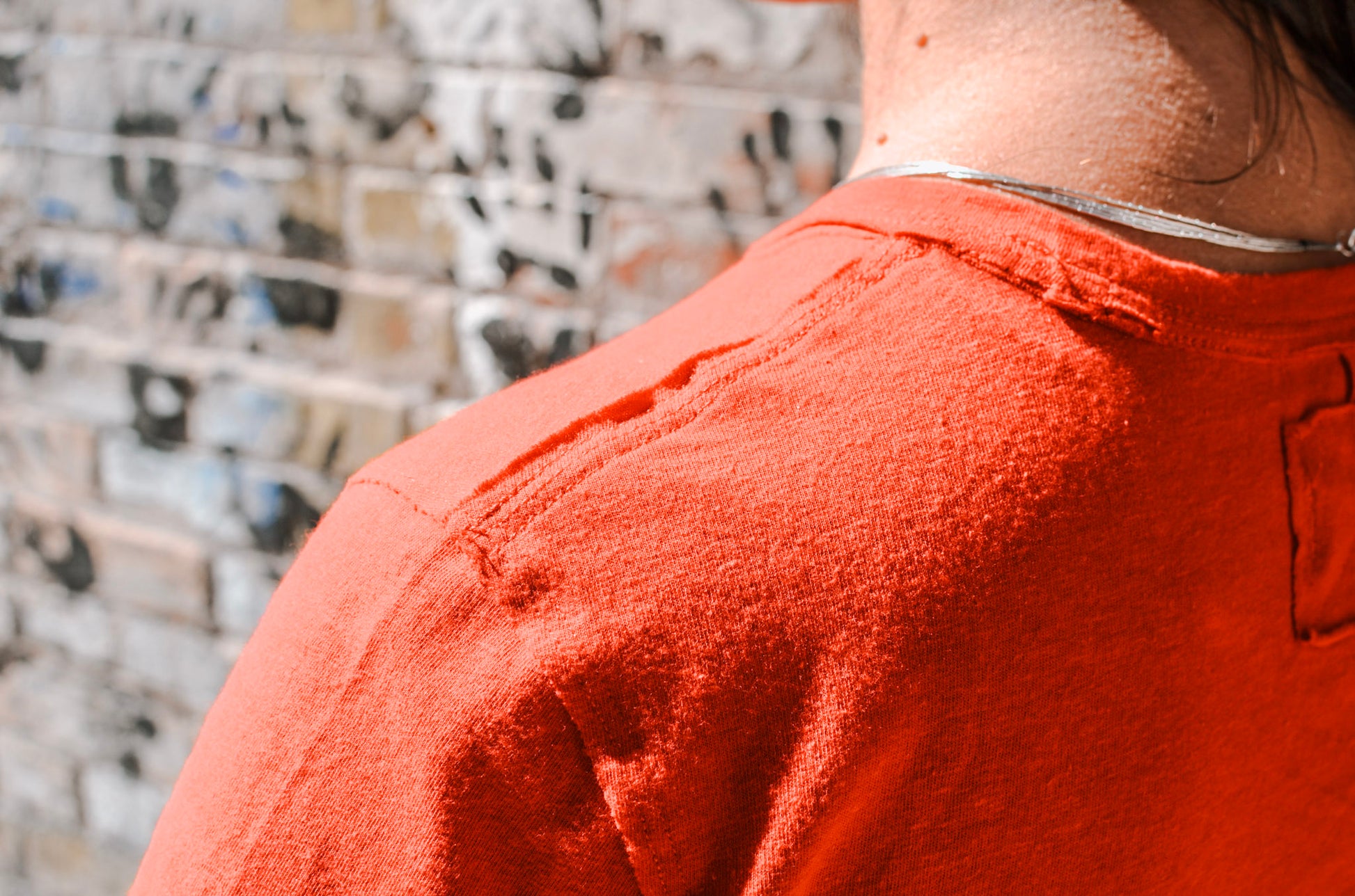 Person wearing an orange shirt with a textured wall in the background
