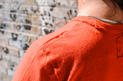Person wearing an orange shirt with a textured wall in the background
