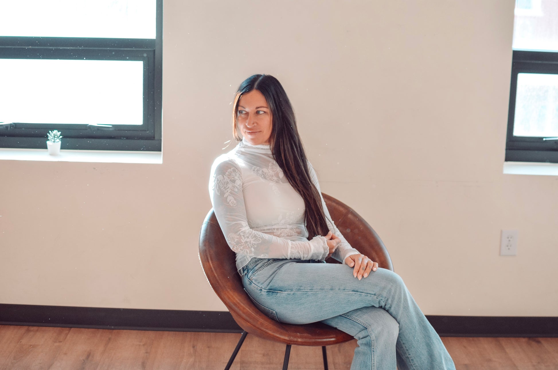 Woman sitting on a chair in a room with large windows and beige walls.