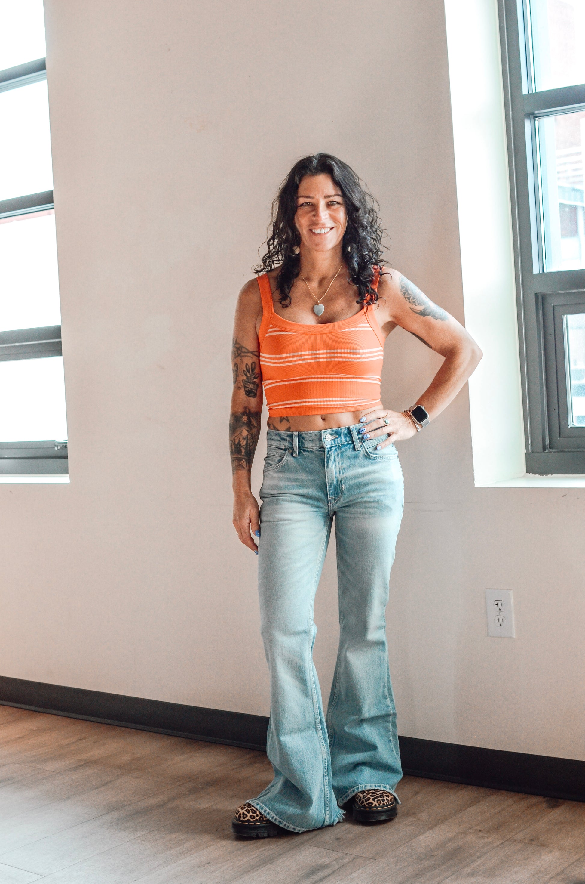 Woman wearing an orange striped tank top and light blue jeans standing indoors.