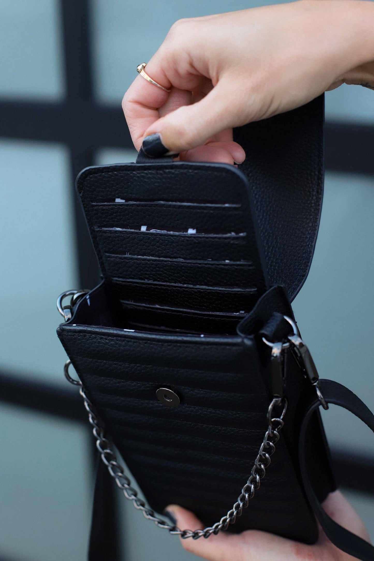 Black leather wallet with chain detail held by a hand against a blurred background