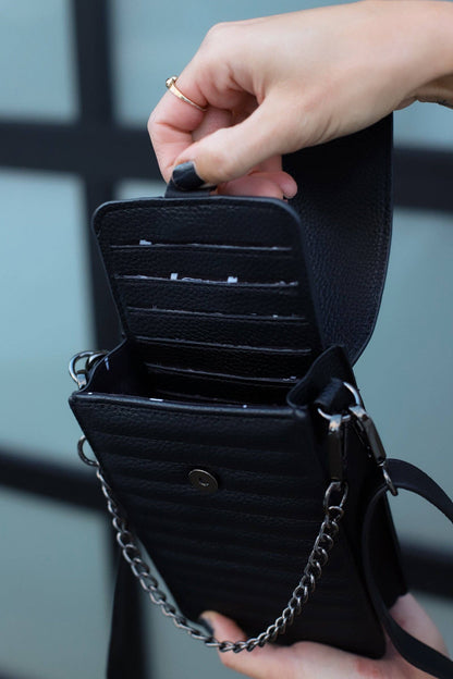 Black leather wallet with chain detail held by a hand against a blurred background