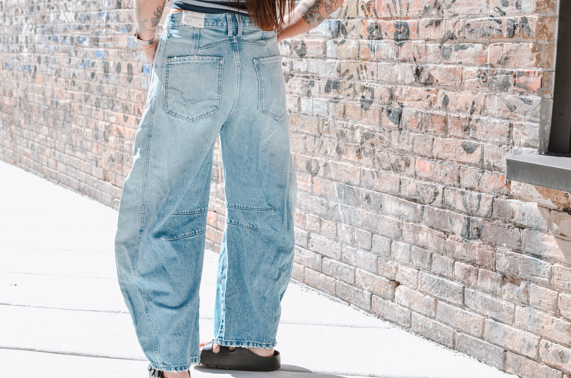Person wearing light blue jeans standing against a stone wall.