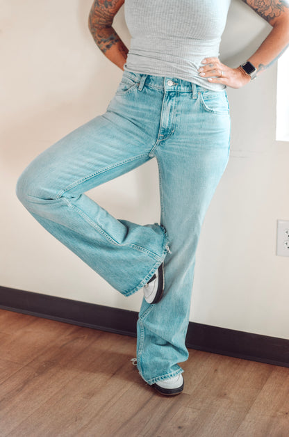 Person wearing light blue jeans and a gray top, standing on a wooden floor.