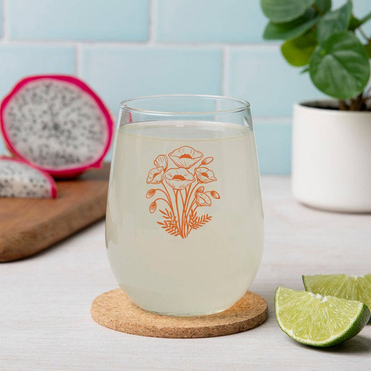 Clear glass with floral design on a cork coaster, dragon fruit, lime, and plant in the background.