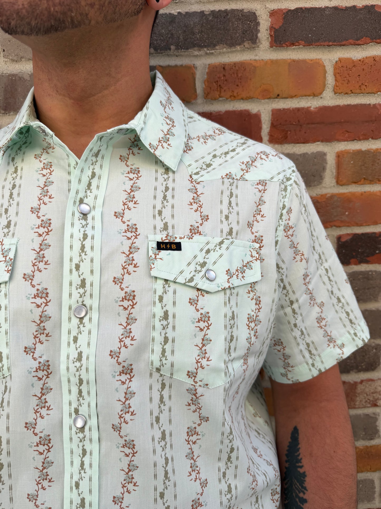 Close-up of a person wearing a floral-patterned shirt against a brick wall.