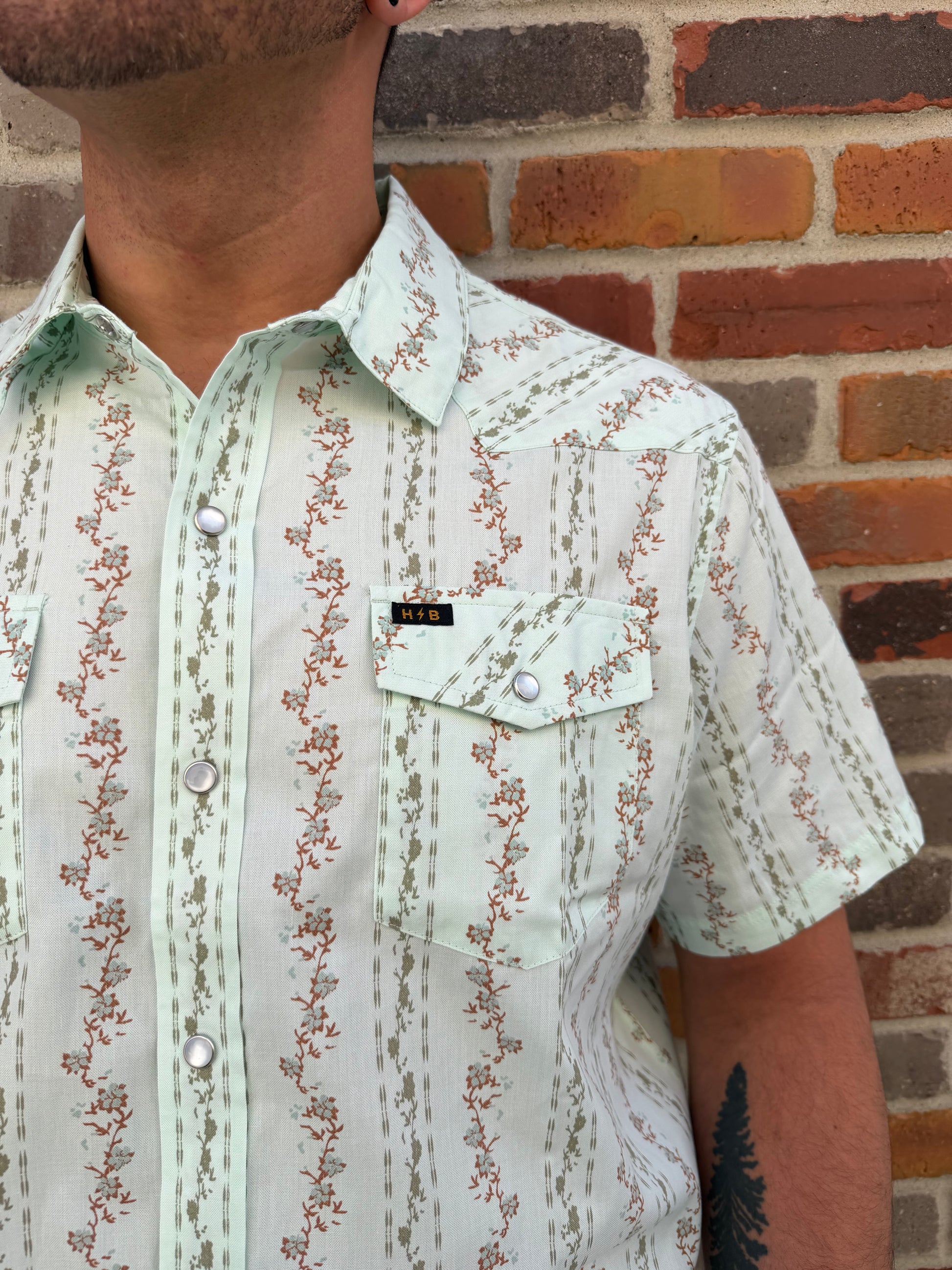 Close-up of a person wearing a floral-patterned shirt against a brick wall.