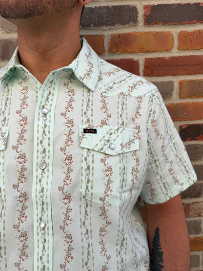 Close-up of a person wearing a floral-patterned shirt against a brick wall.