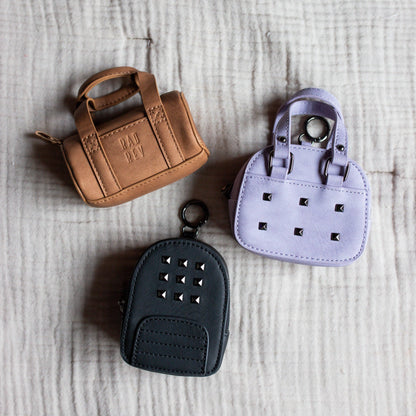 Three small handbag-shaped keychains on a textured surface
