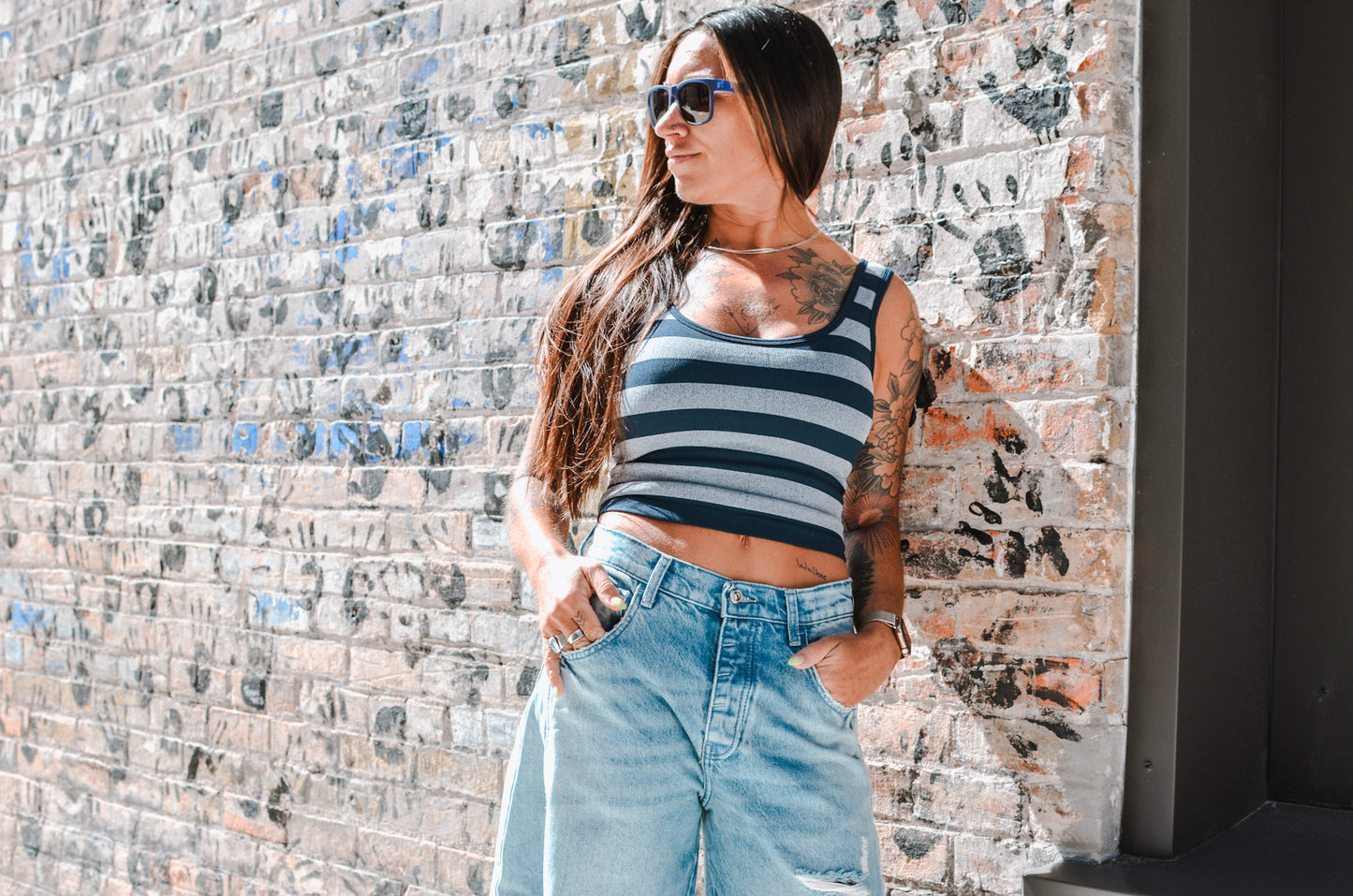 Woman wearing a striped tank top and ripped jeans against a textured wall.