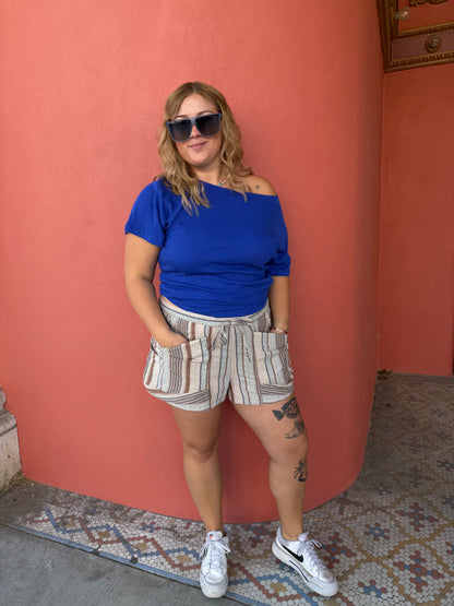 Person wearing a blue top and patterned shorts standing on a red couch.
