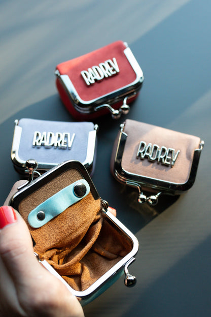 Four small leather bags with 'RADREV' branding on a reflective surface.