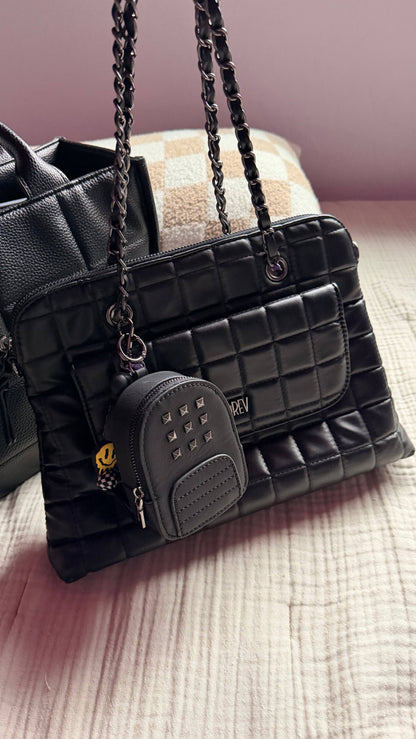 Black quilted handbag with a smaller matching pouch on a textured surface.