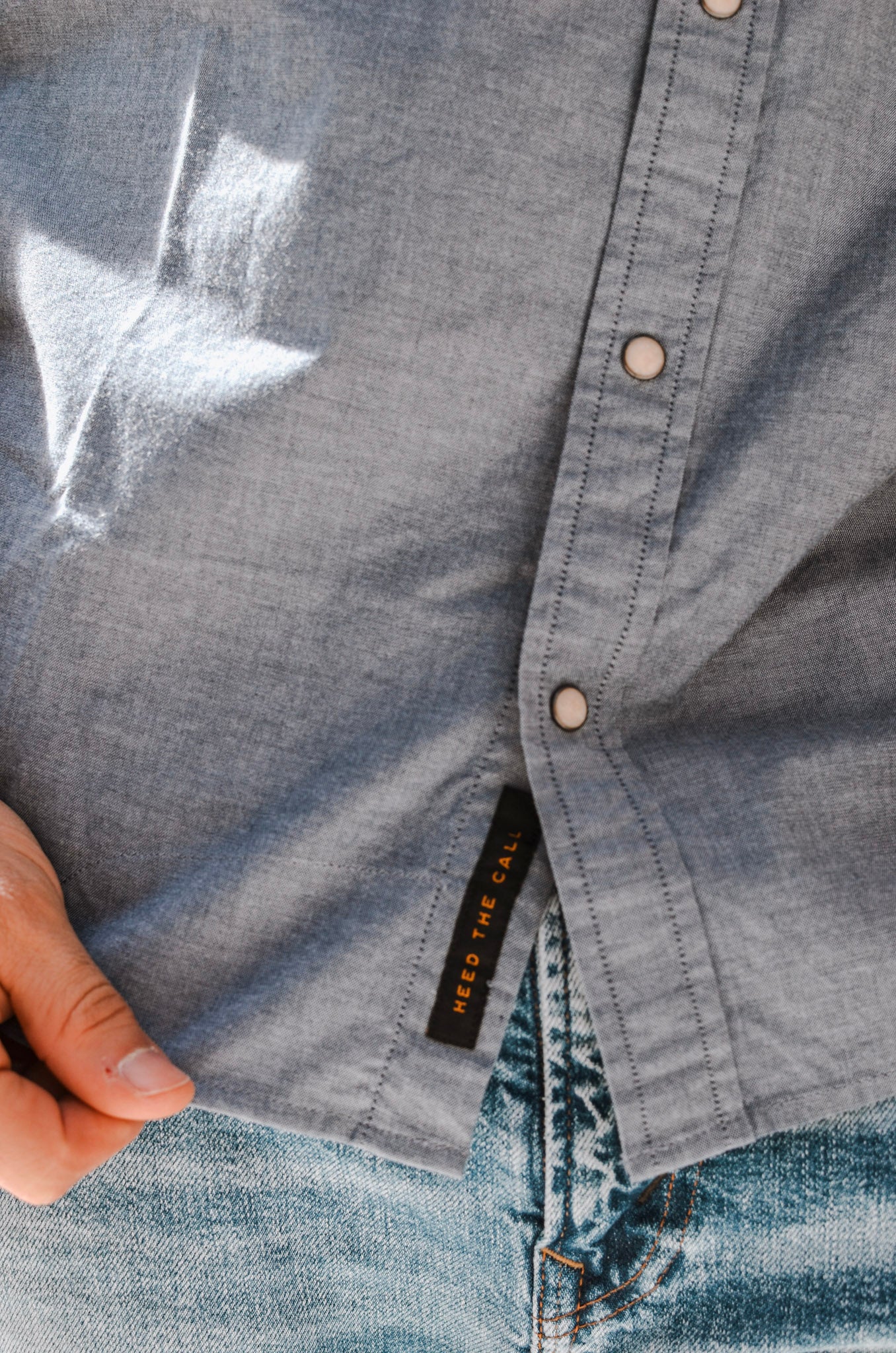 Close-up of a denim shirt with a brand label being held by a hand.