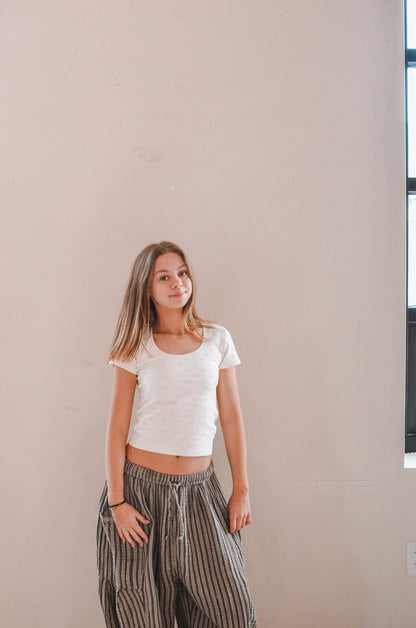 Woman wearing a white top and striped pants standing against a plain wall.