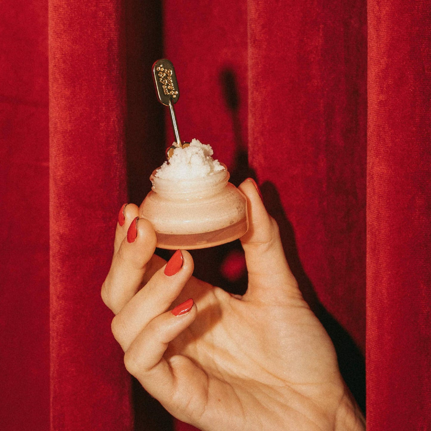 Hand holding a small dessert with a spoon against a red curtain background