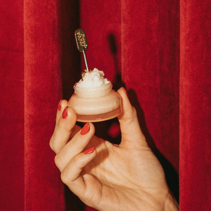 Hand holding a small dessert with a spoon against a red curtain background