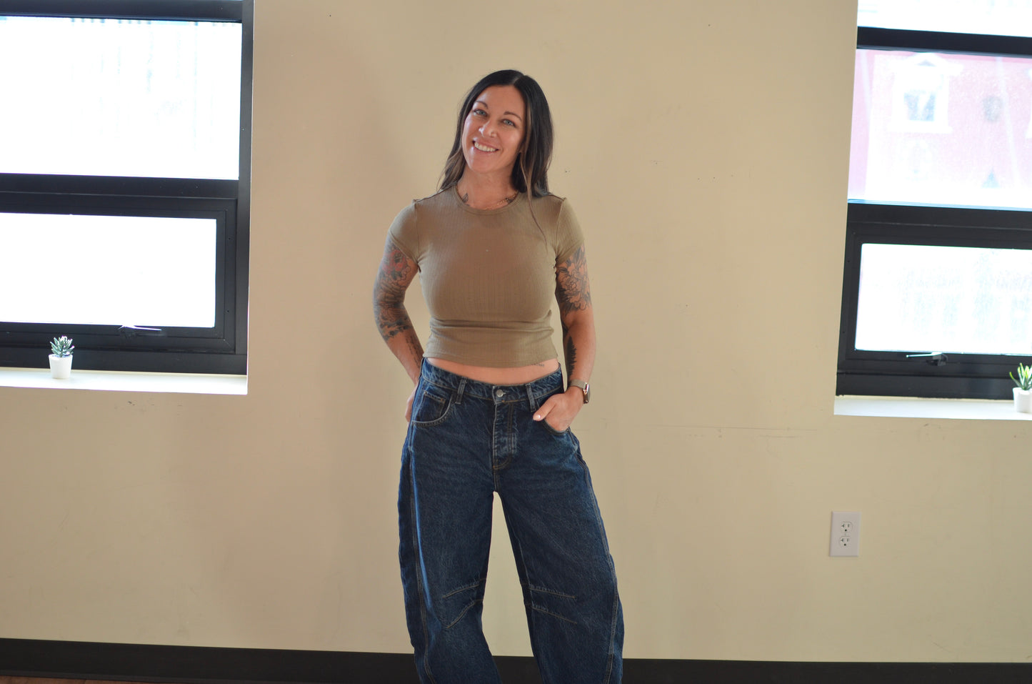 Woman standing in a room with beige walls and windows.