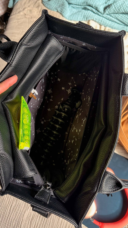 Black bag with a green snack packet inside, held by a hand.