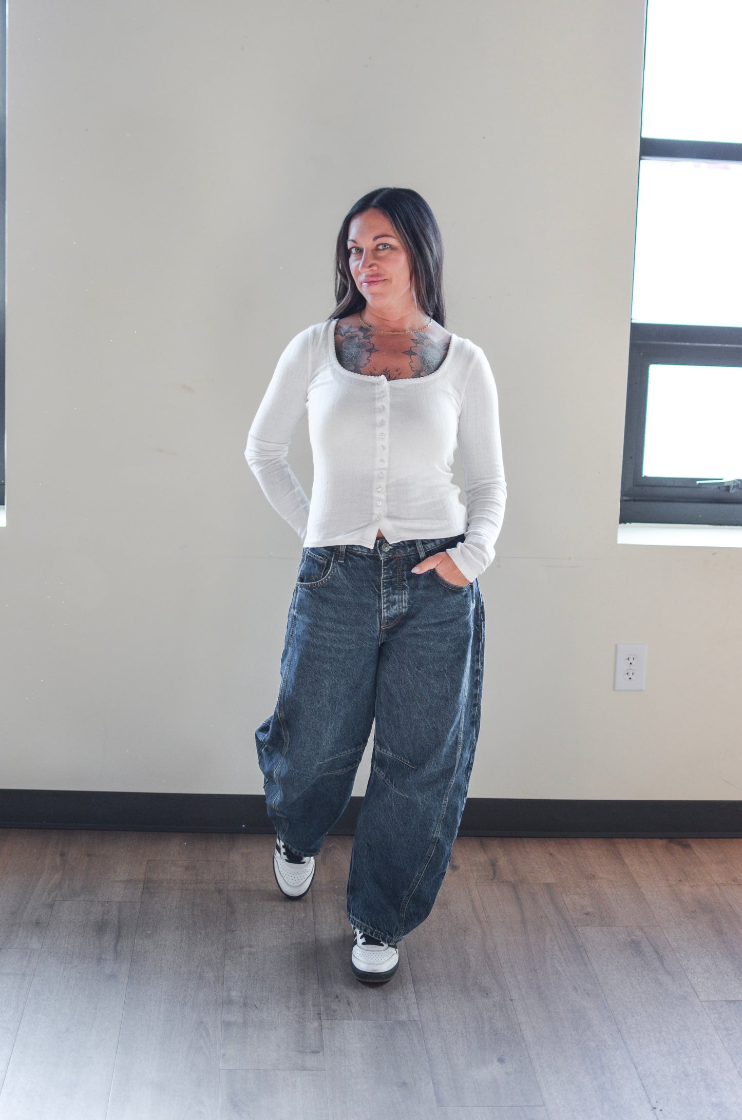 Woman wearing a white cardigan and blue jeans standing in a room with a neutral color scheme.