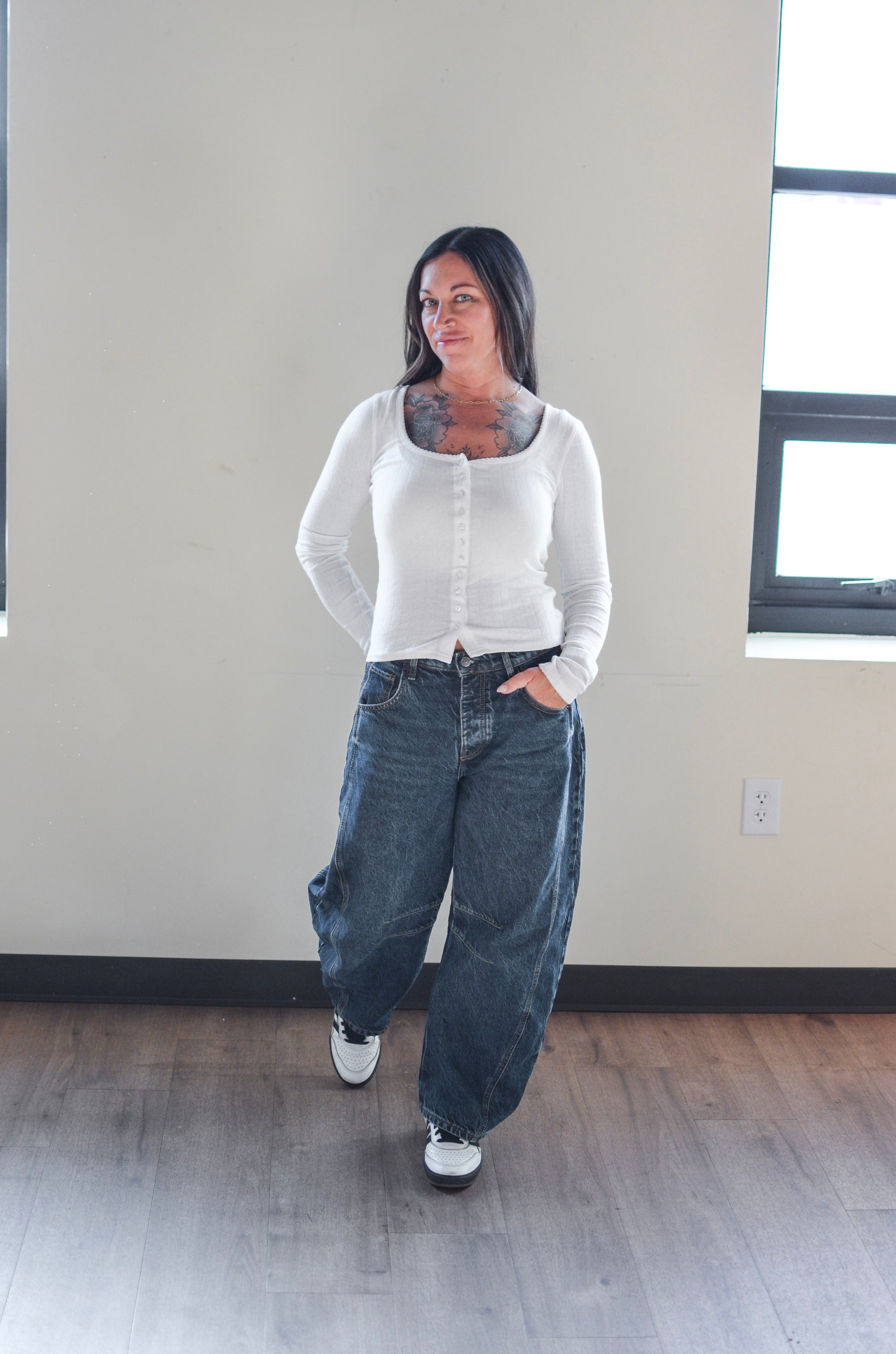 Woman wearing a white cardigan and blue jeans standing in a room with a neutral color scheme.