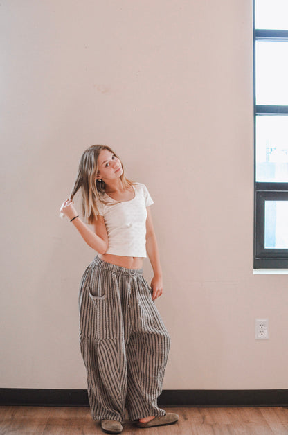 Woman wearing a white top and striped pants standing in a room with a neutral wall and window.
