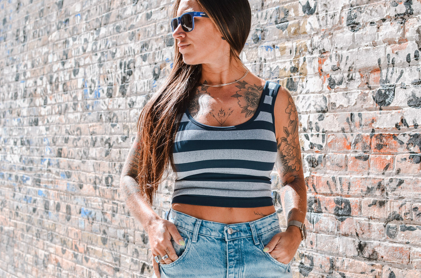 Woman wearing a striped tank top and sunglasses against a textured wall.