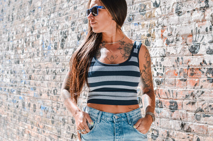 Woman wearing a striped tank top and sunglasses against a textured wall.