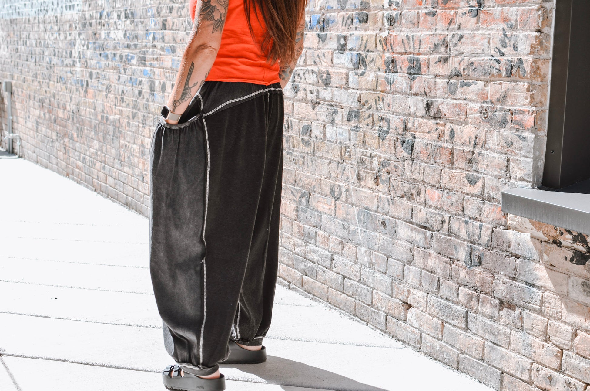 Person wearing black pants with white piping against a brick wall.